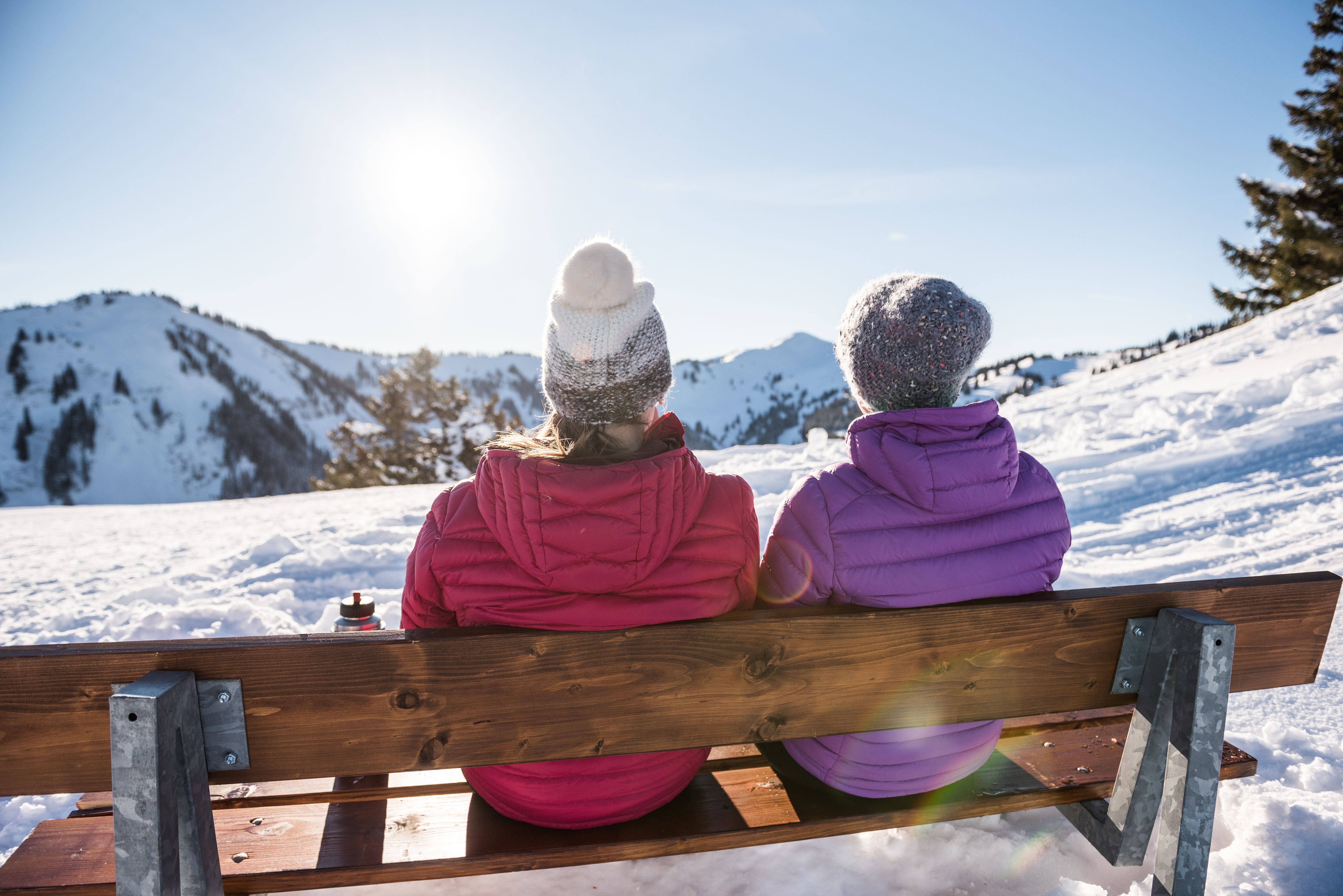 Zwei Frauen sitzen auf einer Bank inmitten einer Schneelandschaft in Bolsterlang in den Hörnerdörfern im Allgäu und blicken in die Berge.